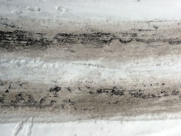 Road texture with thin layer of snow on surface and dark tire marks.
